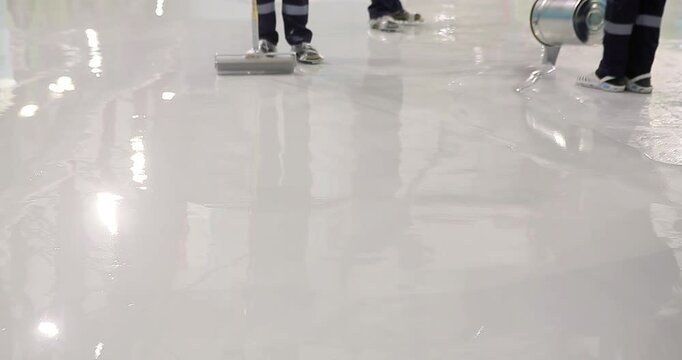 A construction worker works Spiked Roller on a construction site. A construction worker applies resin floors using a Spiked Roller. The process of creating polymer floors