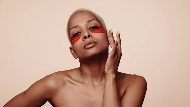 Stunning portrait of a bald fashion model with applying under eye patches on skincare routine against a neutral backdrop.