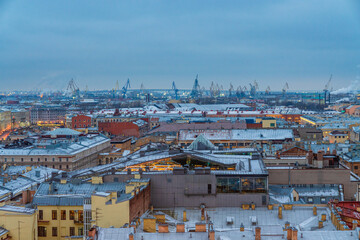 An industrial cityscape with harbour cranes rising behind the buildings in Saint Petersburg, Russia, in the evening
