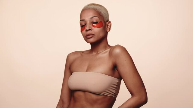 Trendy short hair woman in a strapless top, showcasing a beauty routine with eye patches. Concept of skincare and modern beauty.