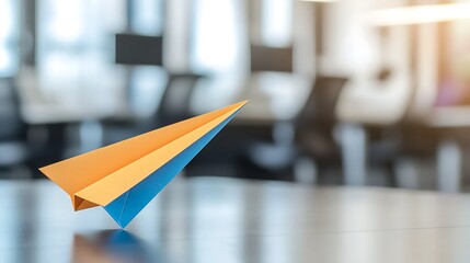 A colorful paper airplane rests on a desk in a modern office space, symbolizing creativity and playfulness in a professional environment.