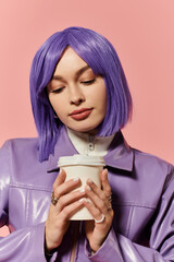 A stylish woman with purple hair sips a warm drink, flaunting her vibrant outfit in soft light.