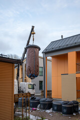 Crane lifting large brown-covered container with trash, surrounded by waste bins and a cluttered...