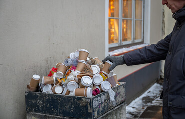 Overflowing trash bin filled with disposable coffee cups and waste, depicting environmental...