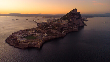Aerial drone view of Gibraltar at sunset. Street lights on. Europa Sports Complex Stadium. Famous travel destination. Bay of Gibraltar. Orange sunset reflecting on water and landscape.  © alexemarcel