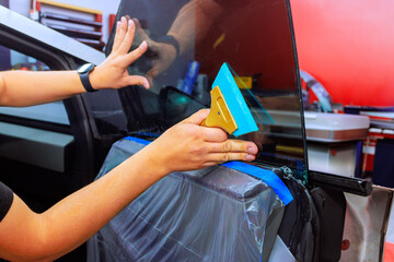 Technician applies window tint to car door while ensuring smooth finish in vibrant auto repair environment.