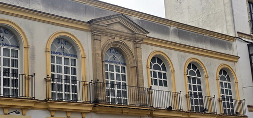 Obraz premium Facade of a historic building with arched windows, wrought iron balconies, and signs indicating tax advisory services; neutral colors and weathered textures on the exterior;