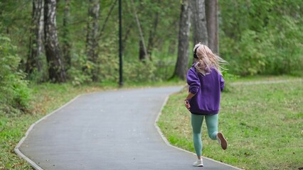 Obraz premium Portrait of young sportswoman jogging during outdoor training in park in the morning. Sport and healthy lifestyle concept