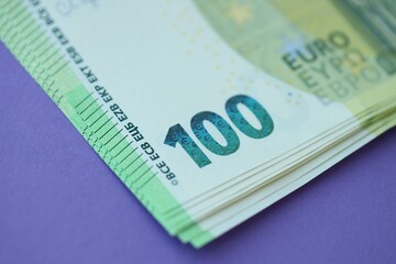 Big amount of one hundred euro money bills on lilac background