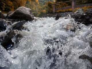 Close-up of a fast-moving mountain river: rushing waters reflecting sunlight and sparkling drops in...