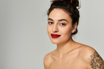 Beautiful woman showcases her striking red lips and floral tattoo in a minimal setting.