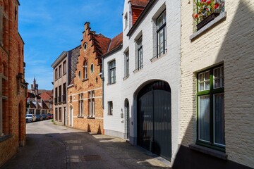 Obraz premium A narrow street with a row of old, historic houses in the city center of Bruges, Belgium. The houses are built in a traditional Flemish style with brick facades and gabled roofs.