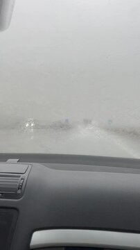 Driving through heavy rain with blurred windshield view, obscured road visibility, and faint traffic lights in a gray, stormy atmosphere