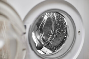 Open door of empty washing machine with metal drum in laundry room