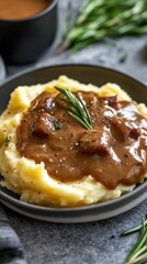 A plate of creamy mashed potatoes topped with savory gravy and meat, garnished with herbs.
