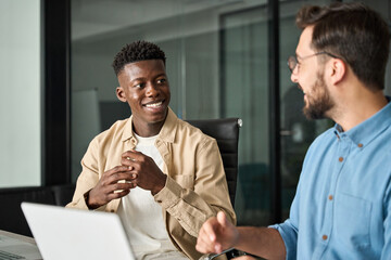 Two busy diverse male employees using laptop computer talking in office. Professional young...