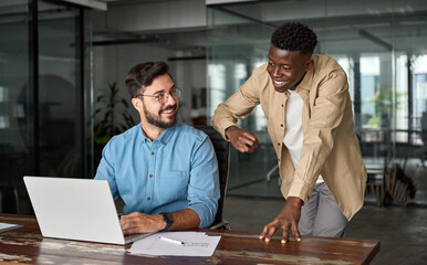 Happy Latin team leader teaching young male African coworker explaining online project strategy....