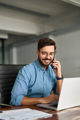 Busy happy young Latin business man talking on phone using laptop computer in office. Smiling...