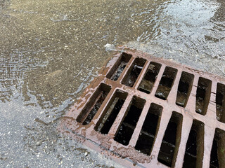 Rainwater flows into the sewer drain. Rusty sewer drain grate