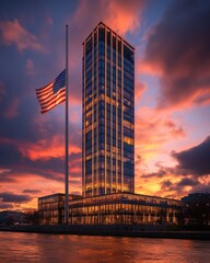 Modern skyscraper at dusk with american flag at half-mast against dramatic sunset sky