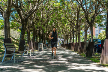 Athletic young man enjoying a refreshing run under the canopy of leafy trees in the park.