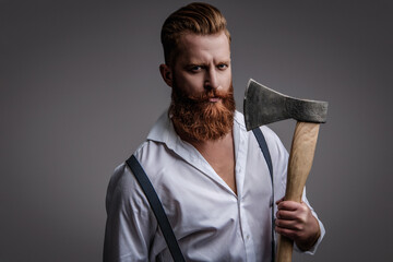 Brutal bearded man in vintage suspenders holding ax isolated on grey