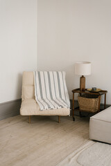 White armchair with a striped blanket, lamp on table clean and simple living room