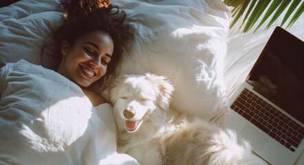 Smiling woman cuddles dog in cozy bedroom with laptop nearby