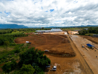 Factory Construction Aerial View: An expansive aerial shot captures a large factory under construction, nestled amidst a landscape of cleared land, lush vegetation.