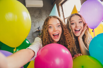 Two young women celebrating together in a colorful living room filled with cheerful balloons