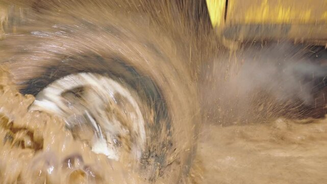 A close-up of an off-road vehicle's wheel and suspension splashing through a muddy puddle, with water and dirt flying everywhere. Extreme mud racing. Slow motion