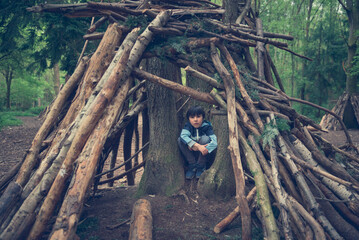 Kid hiding away alone in the forest inside a wigwam branches hut structure, isolated and serene under the protection of the playhouse shelter in the forest. © Alicia