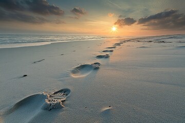 Footprints lead towards a setting sun on a tranquil beach, serene and peaceful.