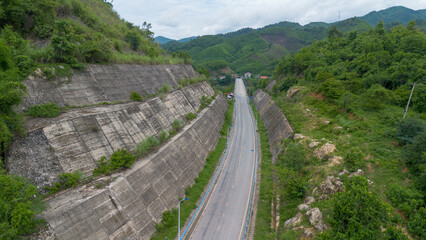 Winding Road Through the Mountains: An aerial perspective of a long, winding asphalt road snaking its way through a mountainous landscape, with lush green foliage lining the sides.