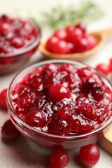 Tasty cranberry sauce in glass bowl and berries on table, closeup