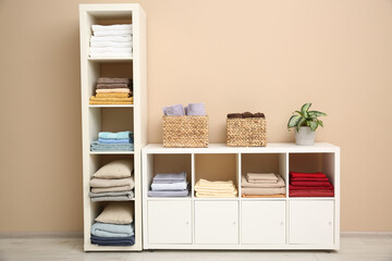 Folded linens, towels and pillows on shelving unit near beige wall. Home textile storage