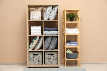 Home textile organization. Different pillows, linens towels and blankets on shelving units near beige wall