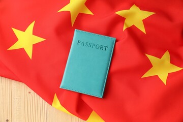 Passport in light blue cover and flag of China on wooden table, top view