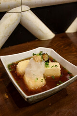 Crispy agedashi tofu cubes sit in a savory broth, topped with grated radish, chopped green onions,...