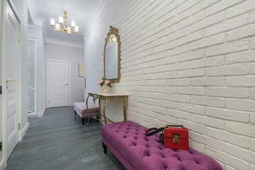A bright hallway with a white brick wall. Soft ottomans and a mirror in the original frame .above...