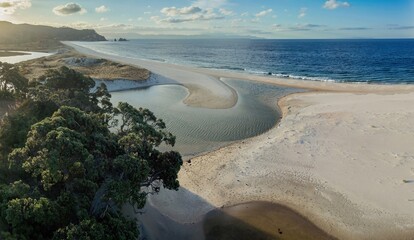 Coastal New Zealand scenery at sunset. Tranquil estuary meets the ocean. Sunlight highlights the...