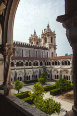 Obraz premium picturesque view through a stone archway, showcasing the architectural grandeur of a historic monastery with its ornate facade, intricate details, and a lush green courtyard