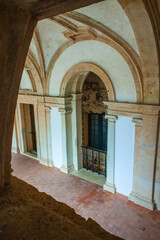 Fototapeta premium captivating perspective through an arched opening, revealing a serene cloister with a series of arches, columns, and a glimpse of a balcony beyond, creating a sense of depth and mystery.