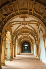 view down a long, arched corridor with a vaulted ceiling, illuminated by natural light streaming through a window, creating a sense of mystery and grandeur within the historic building