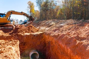 Heavy excavator digs trench for drainage pipe at construction site during excavation work