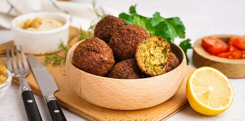 Wooden bowl with delicious falafel balls and lemon on light background, closeup