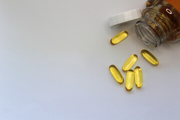 close-up of orange  capsules omega 3 vitamin tablets scattered on a white background next to a jar...