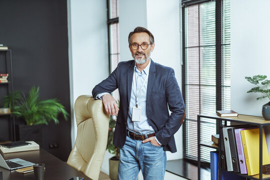 Man in a suit and tie stands in front of a desk with a laptop on it. He is wearing a name tag