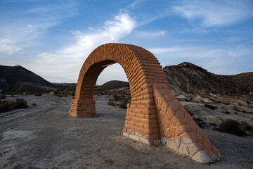 Historic Brick Archway in Desert Landscape: A Freestanding Reddish-Brown Structure Amidst Rolling Arid Hills, Capturing the Unique Blend of Human-Made Architecture and Natural Desert Beauty