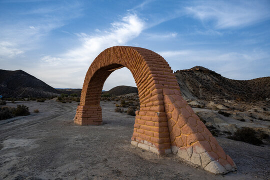 Historic Brick Archway in Desert Landscape: A Freestanding Reddish-Brown Structure Amidst Rolling Arid Hills, Capturing the Unique Blend of Human-Made Architecture and Natural Desert Beauty